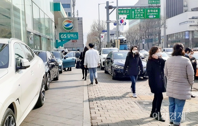 카캐리어에서 하차한 BMW 차량이 인도와 전시장 소유 주차공간을 차지했다. 지하철7호선 내방역 방향으로 가는 주민들이 어깨를 피하면서 불편하게 걷고 있다. 사진=이민섭 기자