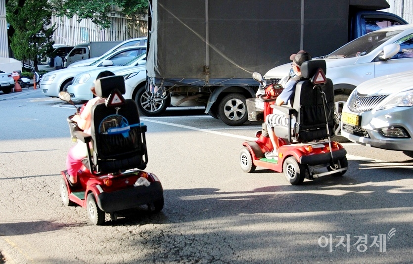 80대로 보이는 노부부가 전동차를 몰고 다정하게 대화하면서 나란히 주행하고 있다. 여기까지는 큰 문제가 없다. 사진=정수남