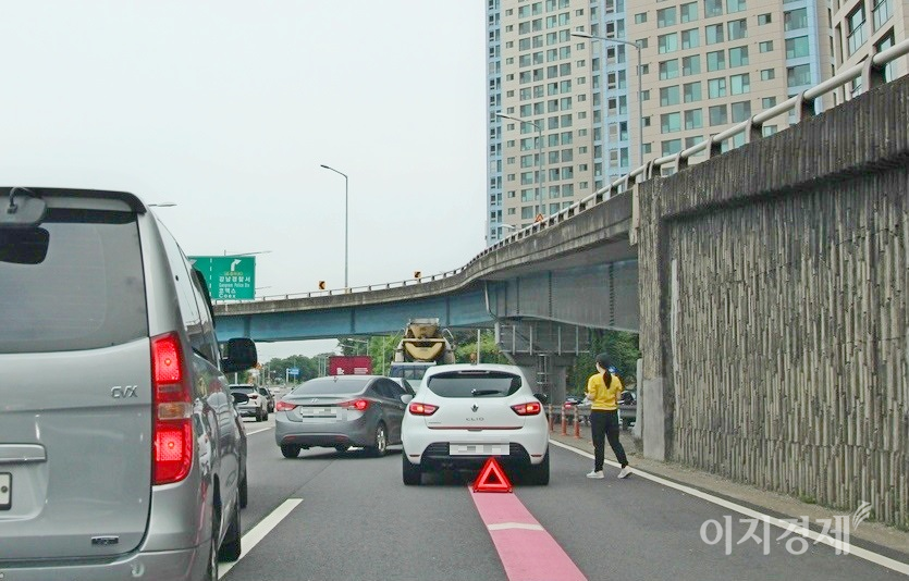 클리오의 여성운전자가 내려 차량 후면에 비상 삼각대를 설치했으나, 차랭과의 간격이 2m 정도로 너무 짧다. 아울러 삼각대 설치 후 수신호나 경광등으로 후속 차량의 서행과 함께 우회를 유도해야 하지만, 휴대폰으로 보험사 비상출동 신고에만 열심이다. 사진=정수남 기자