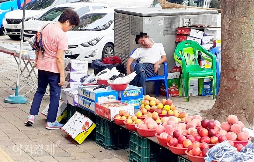 주인장이 35℃에 육박하는 기온에도 아랑곳 하지 않고 고개를 오른쪽으로 떨구고 오수에 빠져 있다. 한 중년 여성 고객이 어찌하지 못하고 과일만 바라보고 있다. 두사람 모두 마스크틀 착용하지 않았다. 사진=정수남 기자