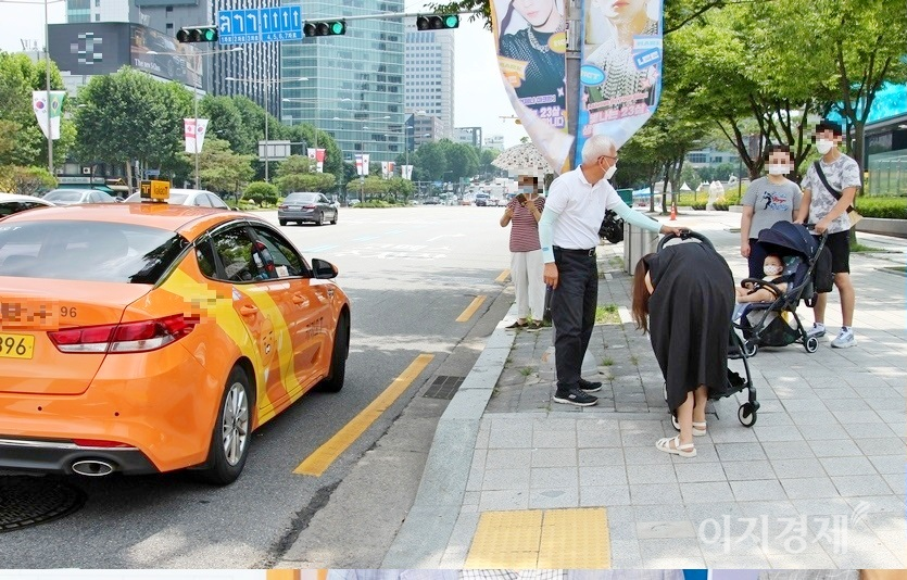 코엑스 앞 택시 정류장에 주황색 서울 택시가 서더니, 백발이 성성한 택시 기사가 내려 운전석 뒷좌석에서 유모차를 꺼낸다. 이어 택시에서 내린 30대 아주머니가 아이를 유모차에 태우고 있다. 이 모습을 본 유모차를 끌고 있는 한 부부가 이 택시를 타기 위해 기다리고 있다. 사진=정수남 기자.