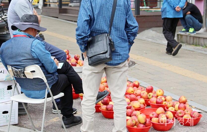 사과 노점상 주인이 사과 판매보다는 로또복권에 더 열심이다. 이 주인이 옆에 선 두 사람과 상의해 번호를 정하더니, 로또 용지에 번호를 기입하고 있다. 바로 앞에 로또판매점이 있다. 사진=정수남 기자
