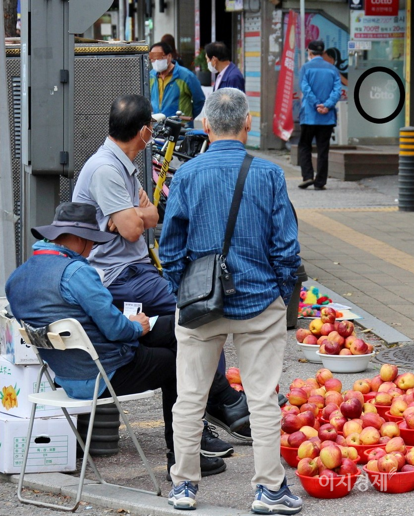 사과 노점상 주인이 사과 판매보다는 로또복권에 더 열심이다. 이 주인이 옆에 선 두 사람과 상의해 번호를 정하더니, 로또 용지에 번호를 기입하고 있다. 바로 앞에 로또판매점이 있다. 사진=정수남 기자