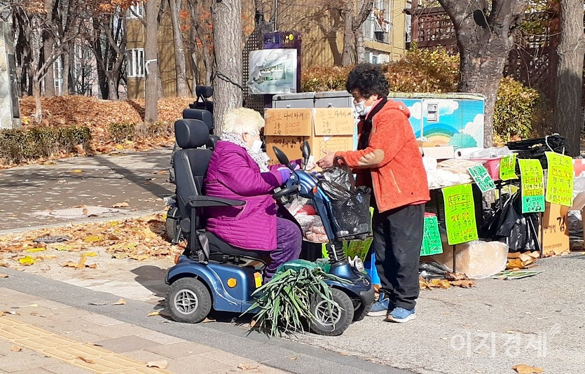 한 노인이 소형 전동차를 타고 노점에서 물건을 구매하고 있다. 사진=정윤서 기자