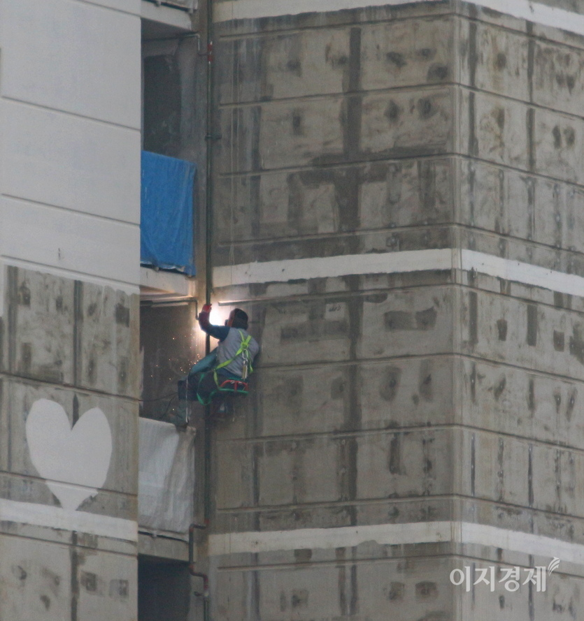 한 아파트 공사장에서 용접공이 동아줄에만 의지해 고층아파트 외벽에서 용접 작업을 진행하고 있다. 사진=이지경제