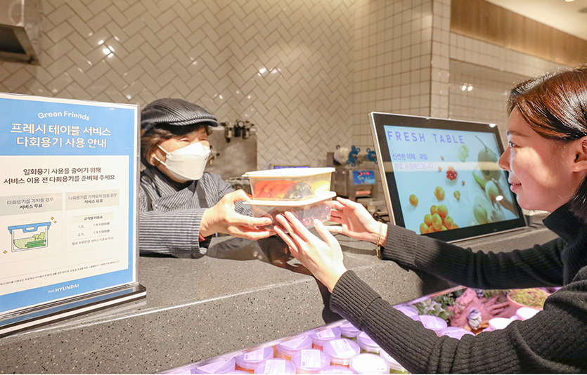 현대백화점 무역센터점 식품관 ‘프레시 테이블’에서 직원이 손님에게 다회용기에 담긴 상품을 전달하고 있다. 사진=현대백화점