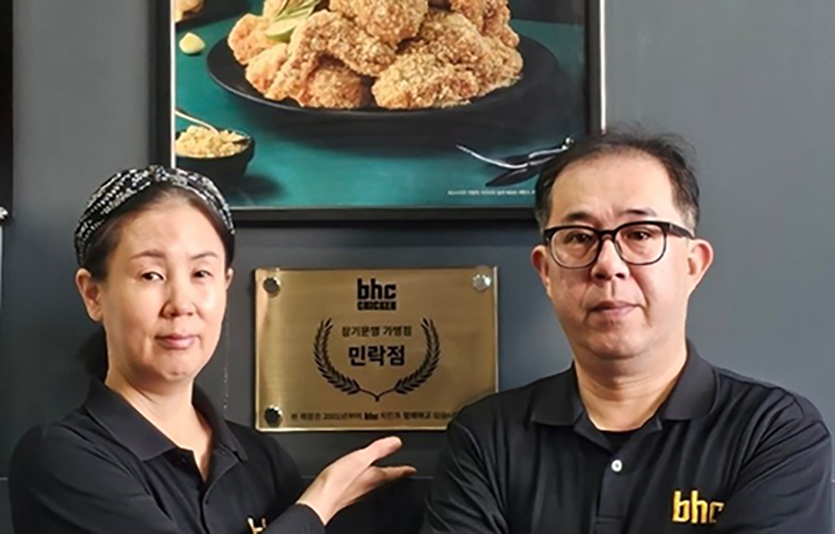 bhc치킨 민락점 신영진 점주 부부가 장기운영 현판 앞에서 포즈를 취하고 있다. 사진=bhc치킨